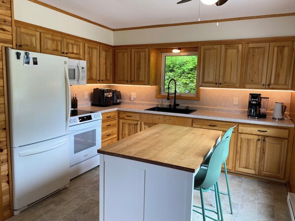Una cocina moderna con armarios de madera, un refrigerador blanco, una estufa, un fregadero y taburetes de bar.