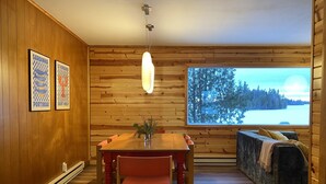 Ein Holzinnenraum mit Esstisch, Stühlen, einer Couch und einem großen Fenster mit Blick auf eine verschneite Landschaft.