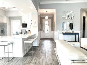 A modern kitchen with white cabinetry, a central island with bar stools, and a grey herringbone floor. - NEW! Renovated & SPARKLING clean single family home with private HEATED pool! (Naples)
