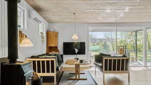Un salon chaleureux avec une cheminée, des meubles en bois, un téléviseur et une vue sur l’extérieur.