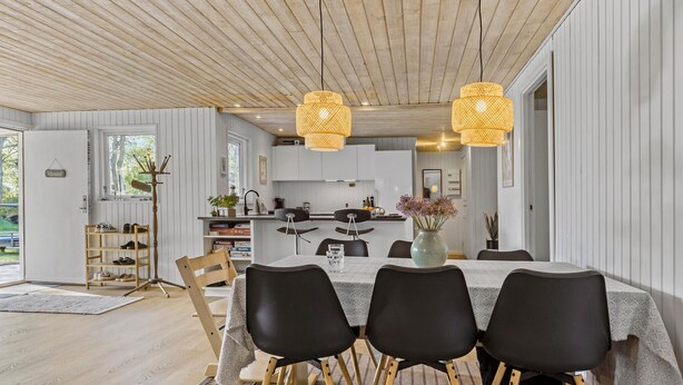 Une cuisine moderne avec des meubles blancs, une table à manger avec des chaises noires et deux suspensions en osier.