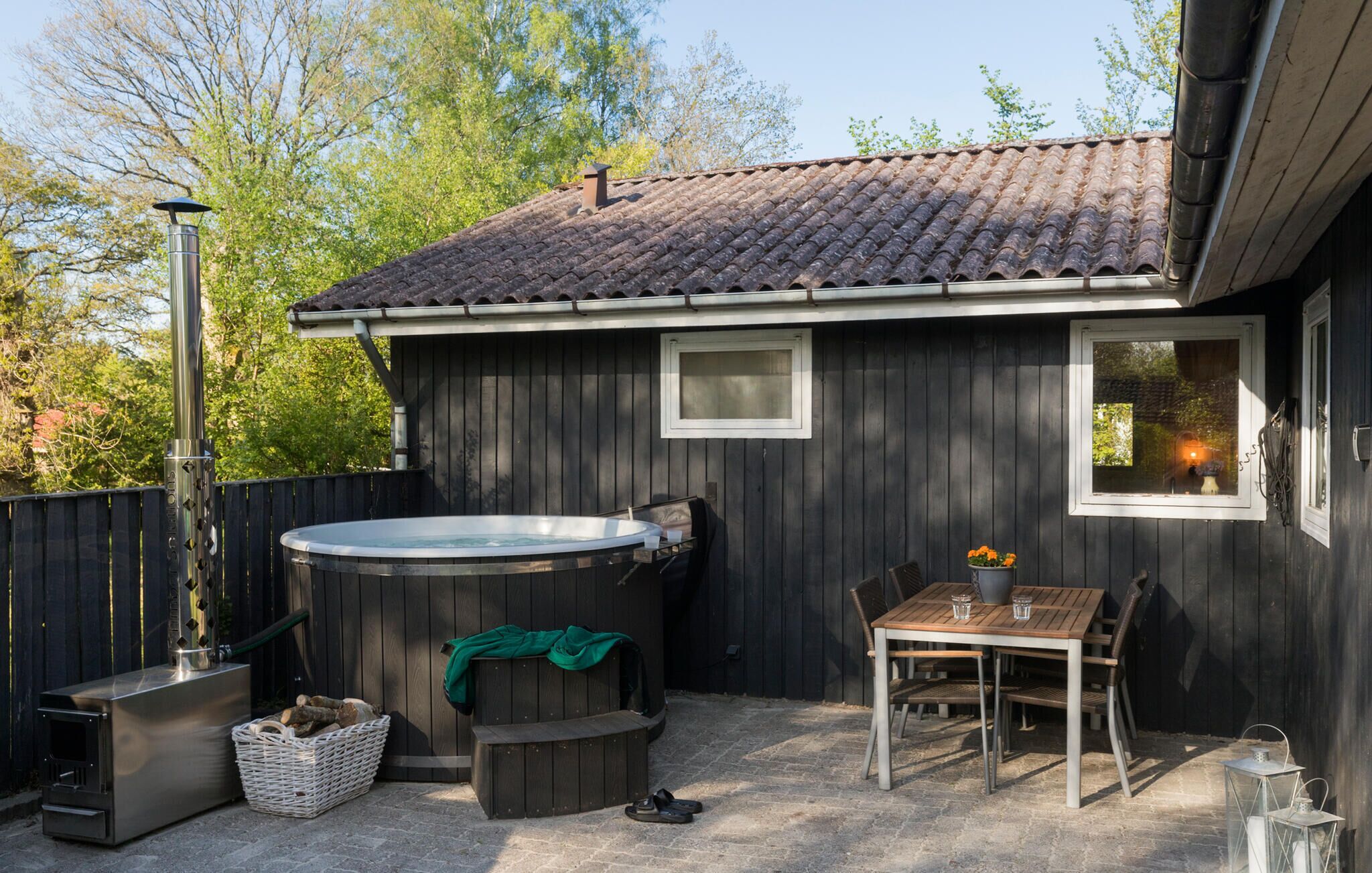 A wooden house with a hot tub, a table with chairs, and a window with a view of trees.