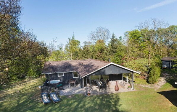Relax in a shaded outdoor space with a patio, hot tub, and barbecue area, surrounded by a well-maintained lawn and mature trees.