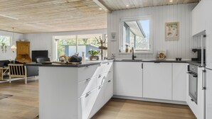 Une cuisine moderne avec des meubles blancs, un plafond en bois et une grande fenêtre qui laisse entrer la lumière naturelle.