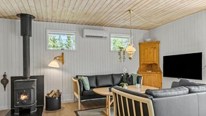 Un salon chaleureux avec un poêle à bois, un canapé, une table à manger et un téléviseur fixé au mur.