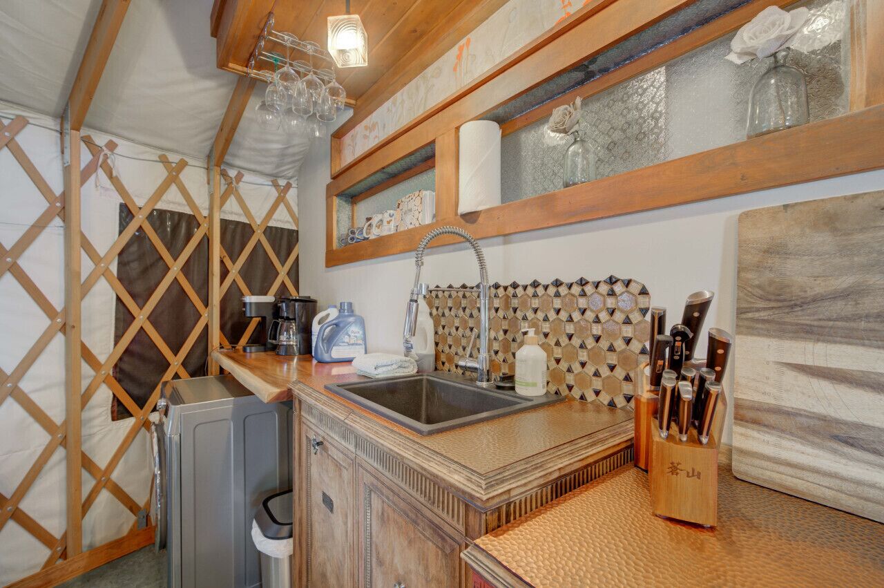 Une cuisine compacte équipée d’un évier, de meubles en bois, d’une machine à café et d’un bloc à couteaux.