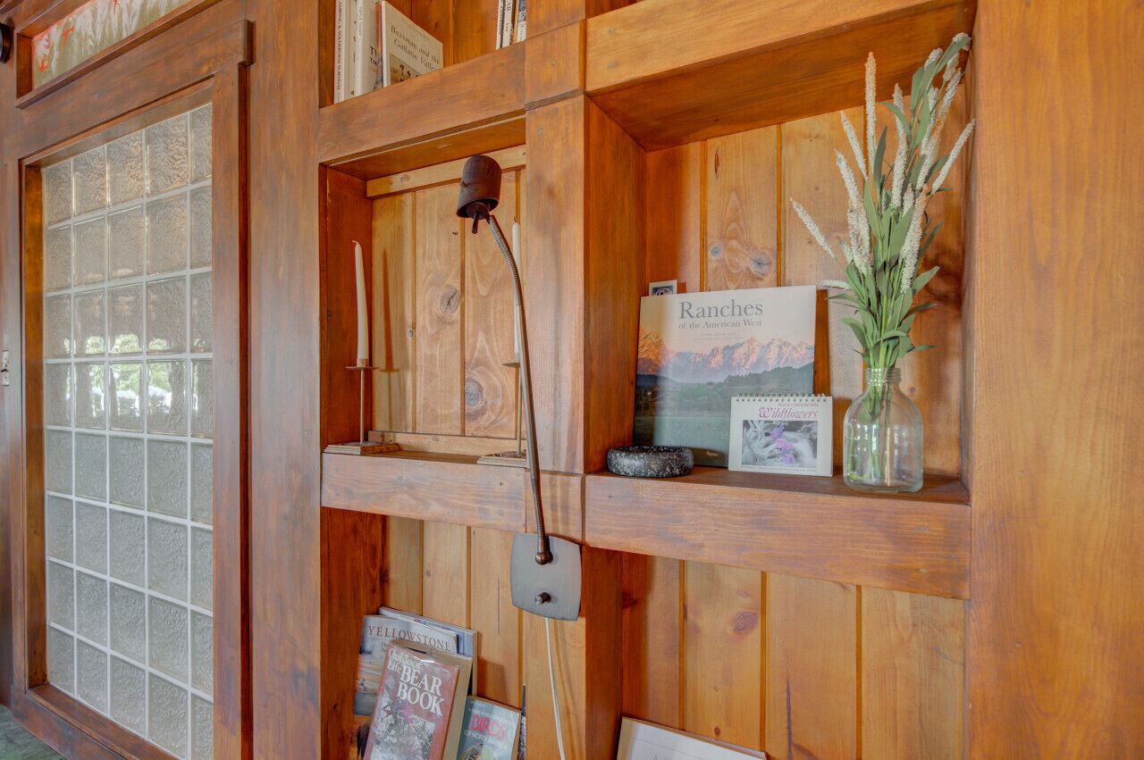 Interior de madera con una estantería que muestra libros, una vela y un florero con plantas.
