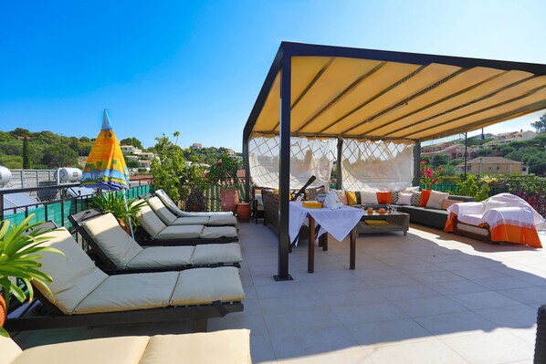 Une terrasse sur le toit avec des chaises longues, un espace salon couvert et des plantes en pot.