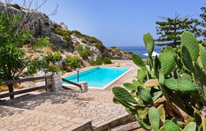 Ein Poolbereich mit freiem Blick auf das Meer, umgeben von Grünflächen und felsigem Gelände.
