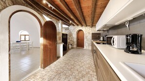 A kitchen with stone walls, wooden beams, a tiled floor, and modern appliances.