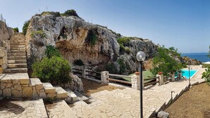 A stone staircase leading up to a rocky cliff with a pool and a lamp post.