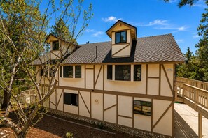 A two-story house with a gabled roof, multiple windows, and a visible address number. - Antelope Retreat - 5BR, Sauna, Foosball Table, Fireplace, Deck, BBQ (Big Bear City)