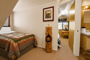 Ein Schlafzimmer mit einem Bett, einer Holzskulptur, einem Gemälde und Blick in einen anderen Raum.