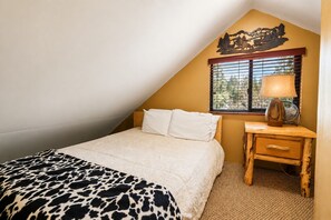 A bedroom with a bed, a nightstand, a lamp, and a window with blinds. - Antelope Retreat - 5BR, Sauna, Foosball Table, Fireplace, Deck, BBQ (Big Bear City)
