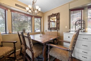 Ein Esszimmer mit Holztisch und -stühlen, einer Kristallleuchter, einem Spiegel und einem Fenster mit Jalousien.