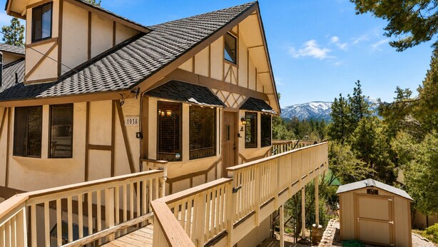 A two-story house with a balcony, a small shed, and a mountain backdrop.