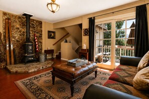 A cozy living room with a stone wall, a fireplace, a staircase, and a view of the outdoors. - Antelope Retreat - 5BR, Sauna, Foosball Table, Fireplace, Deck, BBQ (Big Bear City)