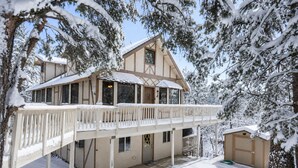 A two-story chalet with a balcony, surrounded by snow-covered trees.