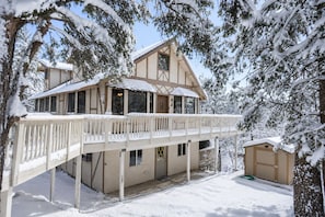 Un chalet de dos pisos con balcón, rodeado de árboles cubiertos de nieve.