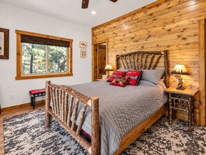 A bedroom with a wooden headboard, a bed with a quilted blanket, two bedside lamps, and a window with a view of trees.