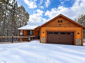 A wooden cabin with a stone foundation, a garage, and a covered porch. - Shem Shack | Luxury Mountain Retreat, Game Room, Wet Bar, Fire Pit & Views (Big Bear City)