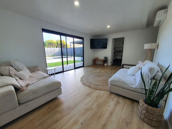 A spacious living room with a large sliding glass door leading to a backyard, a flat-screen TV mounted on the wall, and a cozy seating area with two sofas. - Perfect Large Multi Family Accommodation with Pool (Yarrawonga)