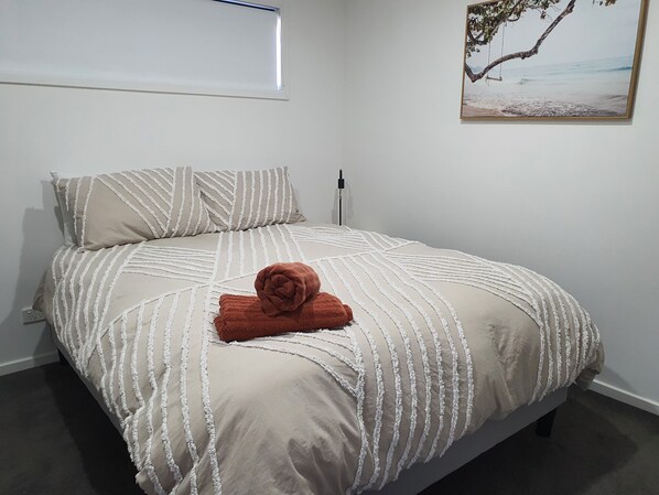 A neatly made bed with striped bedding and a rolled towel, a painting of a tree branch on the wall, and a power outlet on the wall.