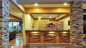 Een receptiebalie met een stenen pilaar, een houten balie en een bord met de tekst 'Cedar Creek Lodge'.