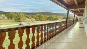 Ein überdachter Balkon mit Blick auf ein Weinberg und Hügel.