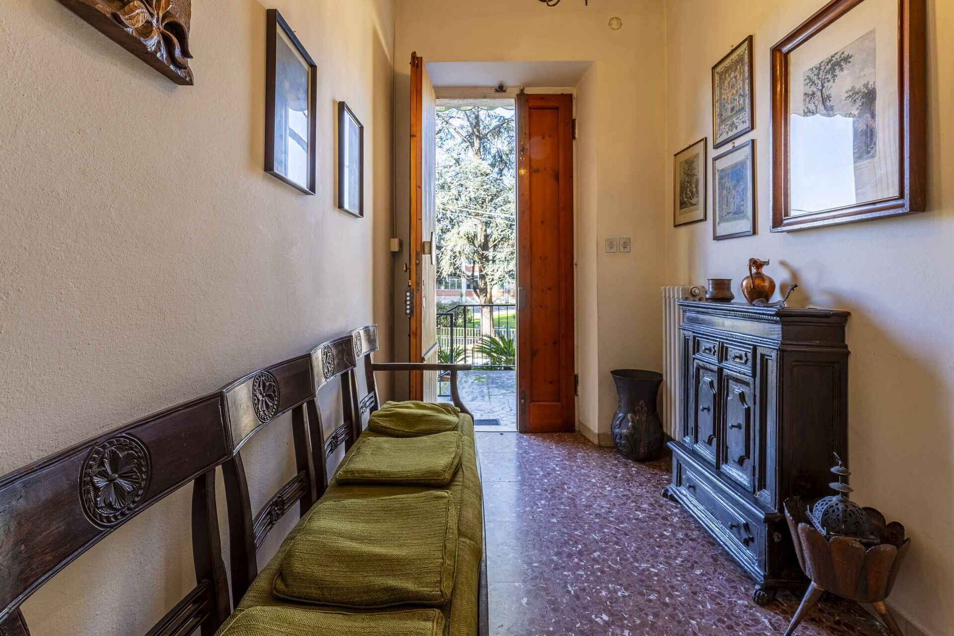 Un couloir avec un banc, une porte en bois et un meuble contenant des objets décoratifs.