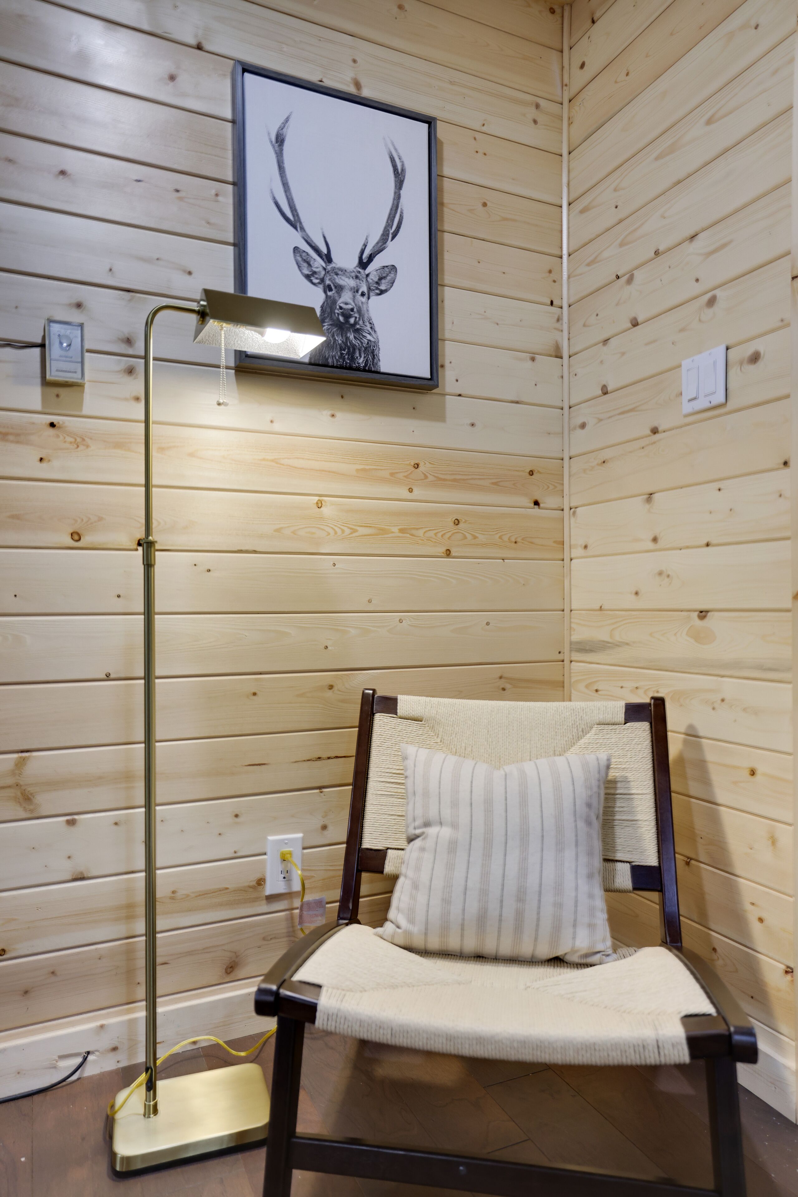 Une pièce aux murs lambrés, avec un lit simple, une lampe de chevet et un tableau représentant un cerf, accroché au mur.