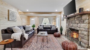 A cozy living room with a stone fireplace, leather sofas, and a large flat-screen TV. - Mins to Skiing! Hot Tub-Fire Pit-Hammock-BBQ-Games (Lake Harmony)