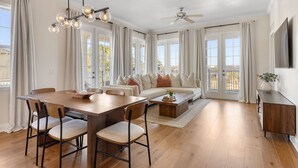 Un salón amplio con una mesa de comedor de madera, sillas, un sofá y una mesa de centro. Hay un ventilador de techo y un televisor montado en la pared.