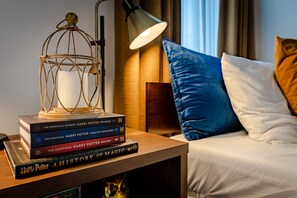 Una pila ordenada de libros de Harry Potter sobre una mesita de noche de madera junto a una cama con almohadas azules y blancas.