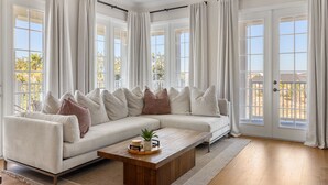 Un salón amplio con un sofá modular grande, una mesa de centro de madera y vistas al exterior a través de amplias ventanas.