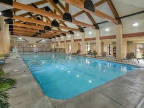 An indoor swimming pool with a concrete floor, wooden beams, and a tiled wall.