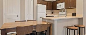 A compact kitchen with a wooden table and chairs, a white refrigerator, and a microwave.