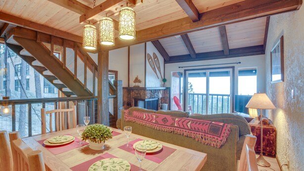 A wooden dining table set with plates, glasses, and a small plant. There is a staircase leading to an upper level, a sofa with a patterned throw, and a lamp on a side table. - 1 Mi to Stagecoach Lift! Homey Tahoe Townhome (Stateline)