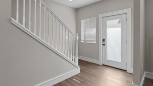 A staircase with white balusters leading to a landing, a door with a frosted glass panel, and a window with blinds.