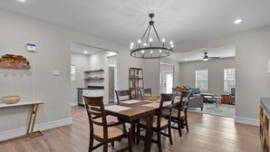 A spacious dining area with a wooden table and chairs, a chandelier, and a view into the kitchen and living room.