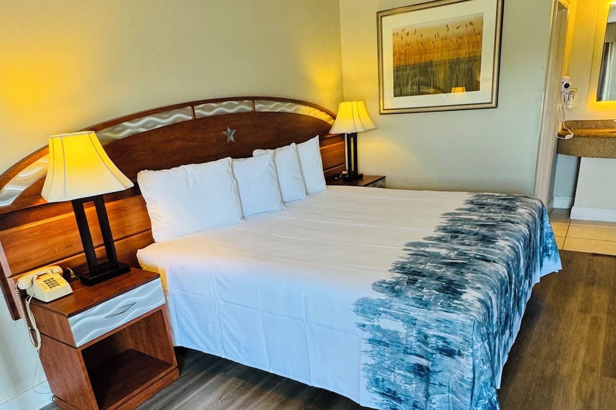 A hotel room with a large bed, wooden headboard, bedside lamps, a bedside telephone, and a framed picture on the wall.