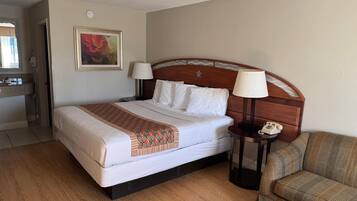 Habitación de hotel con cama, dos lámparas de noche, teléfono, silla y un cuadro en la pared.