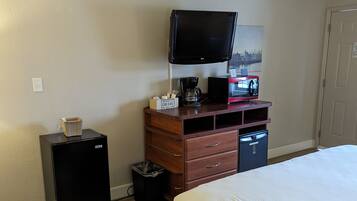 A hotel room with a bed, a TV, a coffee maker, a microwave, and a small desk with a trash can.