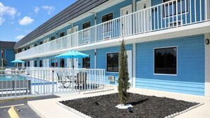 A motel with a pool, outdoor seating, and a small tree in the front yard. - Hotel MonteCarlo (Kissimmee)