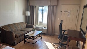 A furnished room with a sofa, a small table, a desk with a chair, a window with curtains, and a door with a 'No Smoking' sign. - Hotel MonteCarlo (Kissimmee)