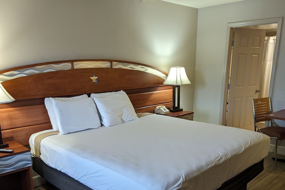 A hotel room with a large bed, wooden headboard, bedside lamp, and a wooden nightstand.