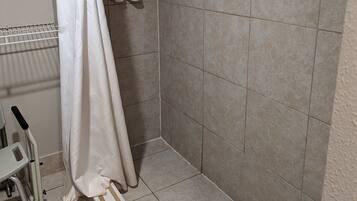 A shower area with beige tiles, a white shower curtain, and a hand soap dispenser on the wall.