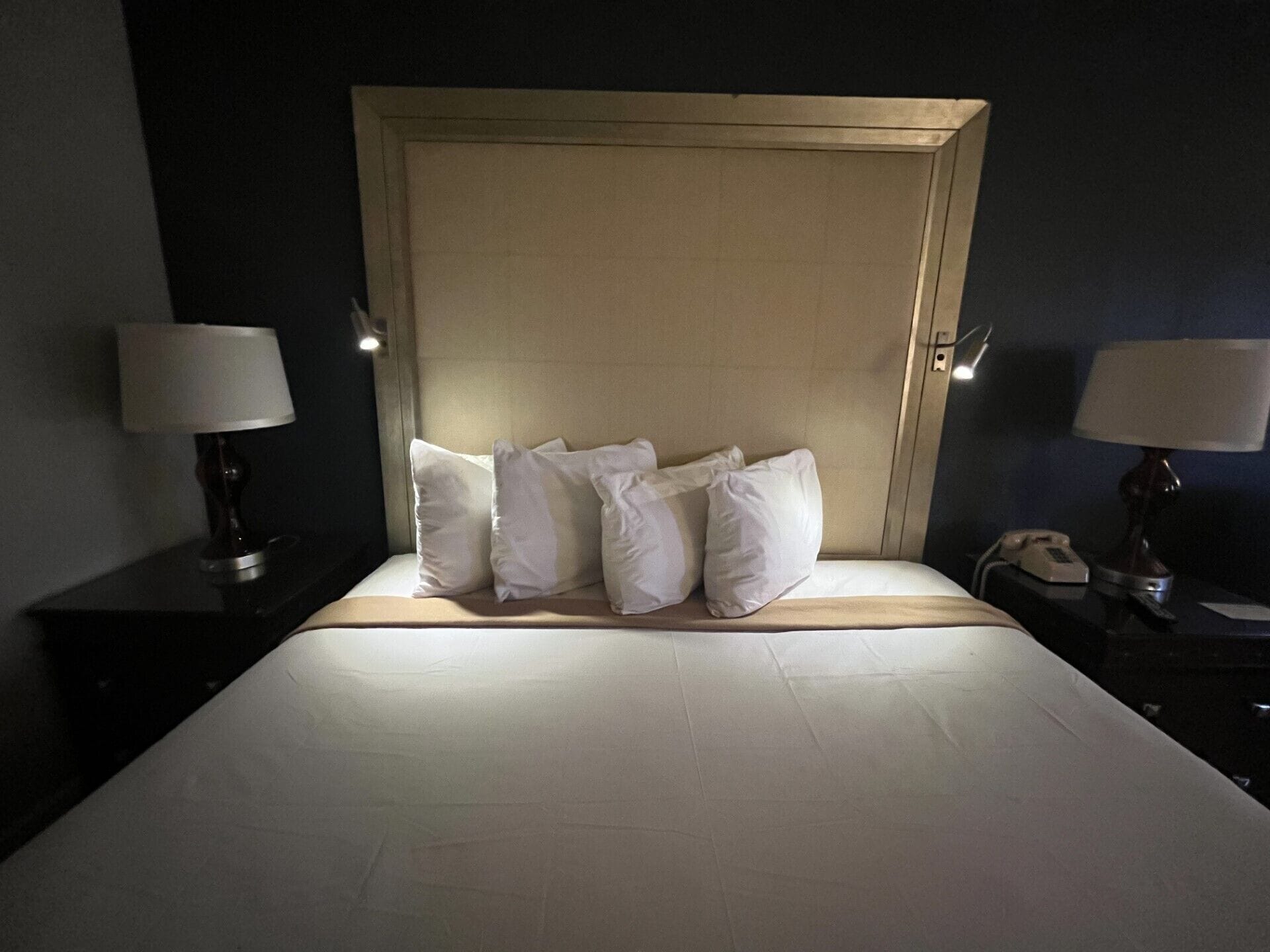A neatly made bed with white linens and pillows, a wooden headboard, and bedside lamps on either side.