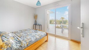 A bedroom with a bed, a small table with a vase, and a sliding glass door leading to an outdoor area with a pool.