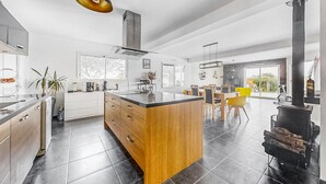 A modern kitchen with a central island, a dining area with chairs, and a large window.